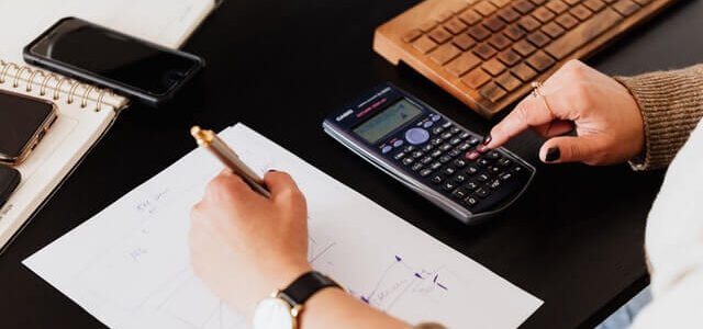 crop woman using calculator and taking notes on paper